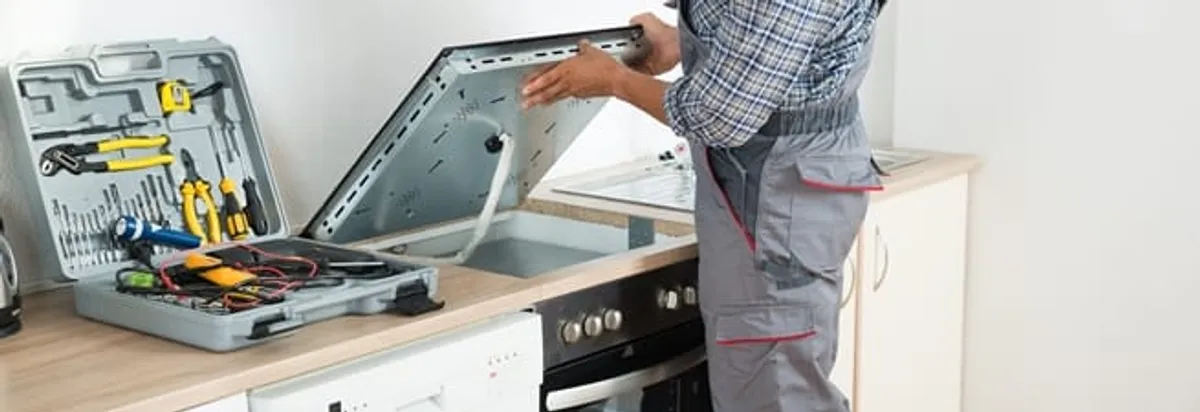 Cooktop repair technician lifting a built-in stovetop for service in Bellevue, WA